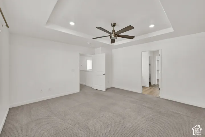 Tray ceiling with recessed lighting and a ceiling fan, light gray carpet flooring, and white walls