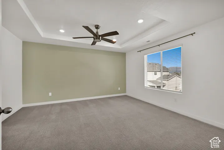 Tray ceiling with recessed lighting and ceiling fan, large window with horizontal blinds, neutral wall colors, and carpet flooring