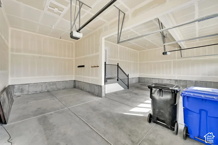 Spacious garage with concrete flooring, automatic garage door opener, and interior staircase with black metal railing