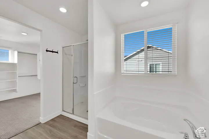 Soaking tub with a window, glass-enclosed shower, wood-finish flooring, recessed lighting, and built-in shelving
