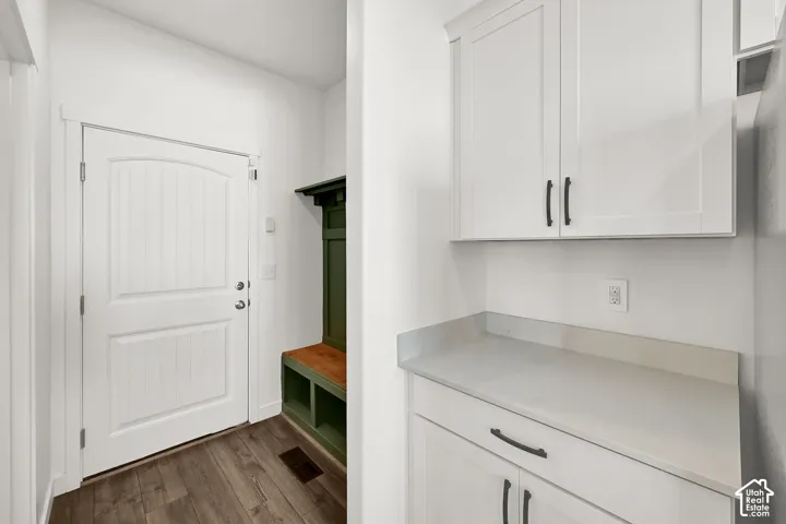 White shaker cabinetry, light-toned countertop, wood-finish flooring, and built-in storage bench