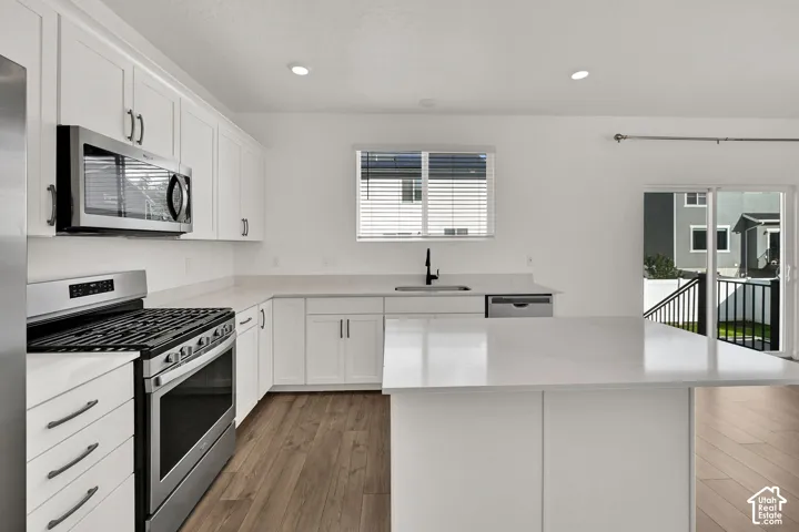 Kitchen featuring white cabinetry, stainless steel appliances, light-toned countertops, wood-finish flooring, and a sliding glass door