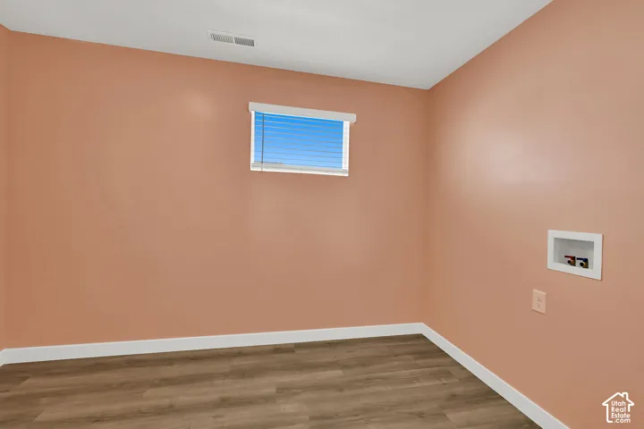 Wood-finish flooring, light peach walls, recessed window with blinds, and laundry connections