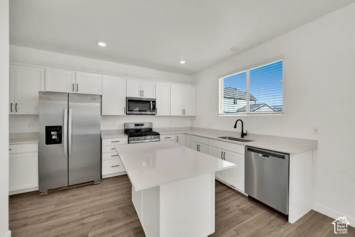 Kitchen featuring white cabinetry, light-toned countertops, stainless steel appliances, a kitchen island, and wood-finish flooring