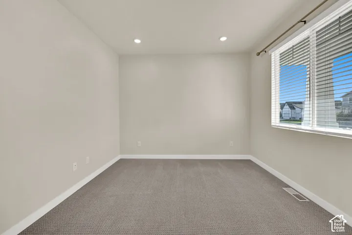 Recessed ceiling lighting, neutral-toned walls, gray patterned carpeting, white window blinds, and white trim
