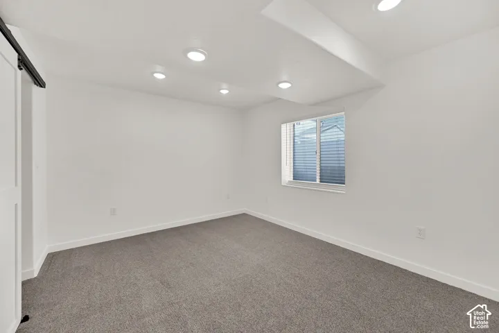 Recessed ceiling lighting, gray carpeting, a window with horizontal blinds, and a white barn door on a black track