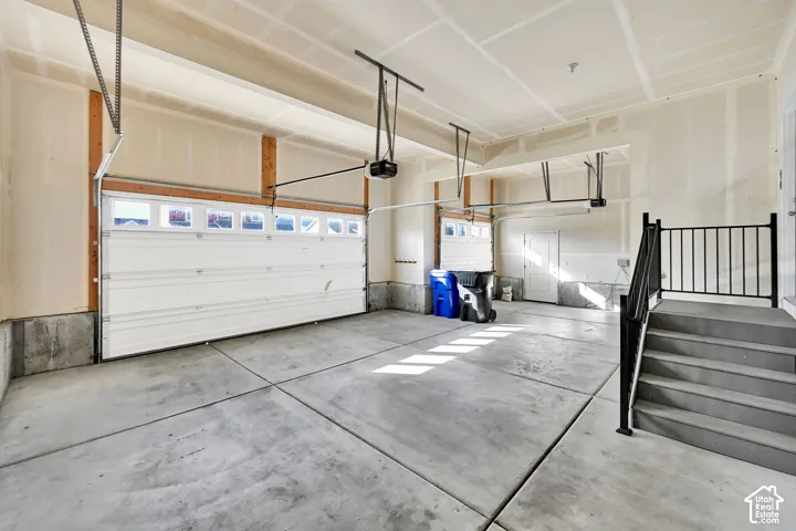 Spacious garage with concrete flooring, two garage doors with window inserts, and built-in stairs with a black metal railing