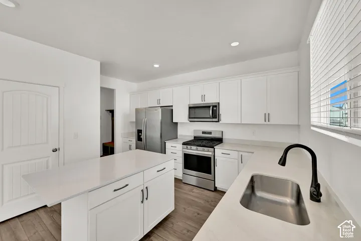 White cabinetry, stainless steel appliances, durable wood-finish flooring, recessed lighting, and a kitchen island with stone countertops