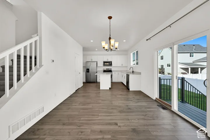 Open concept kitchen with white cabinetry and stainless steel appliances, wood-finish flooring, sliding glass door access to an exterior deck, and a contemporary chandelier