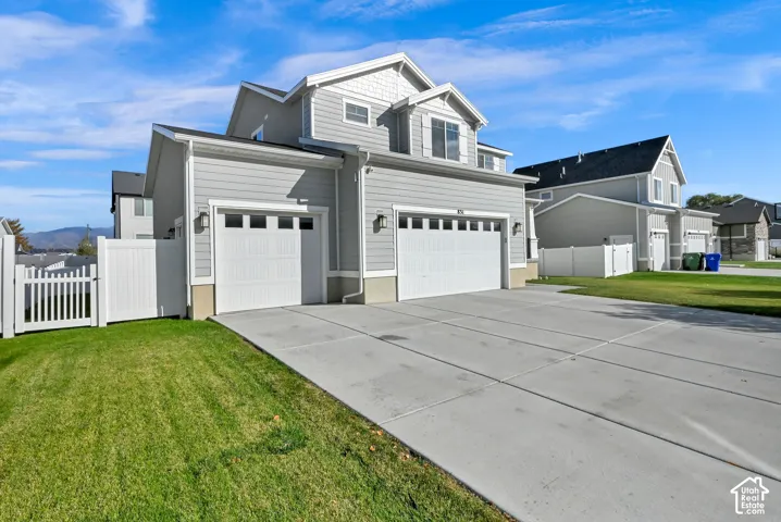 Two-story exterior with light gray siding, white garage doors, a concrete driveway, and a white picket fence