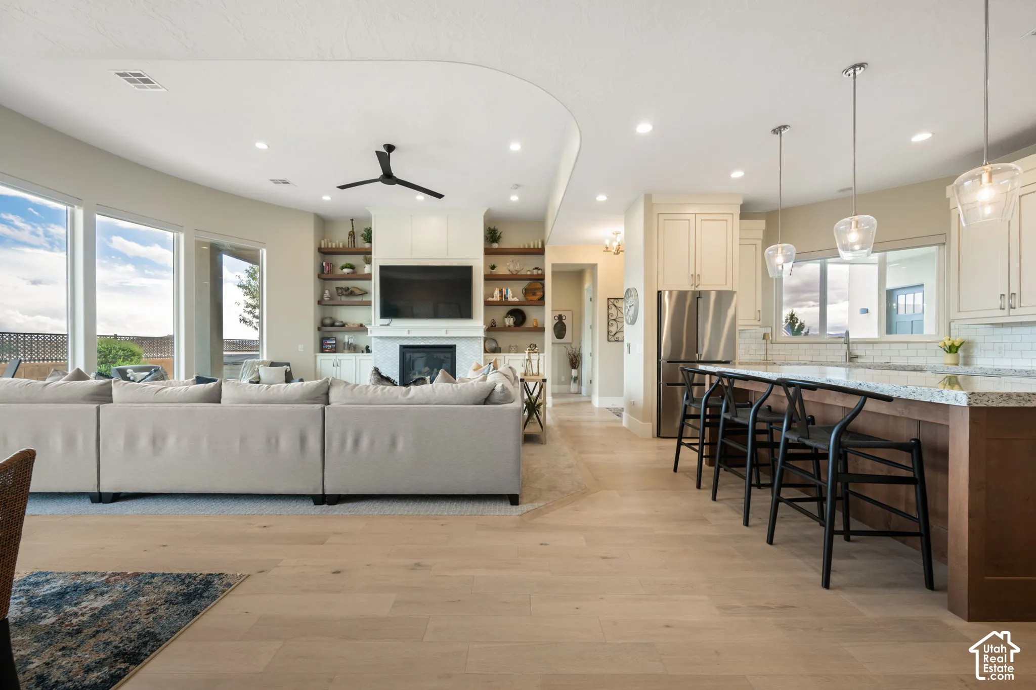 Open-concept living space featuring wood-finish flooring, a kitchen island with seating, stainless steel appliances, and a fireplace with built-in shelving