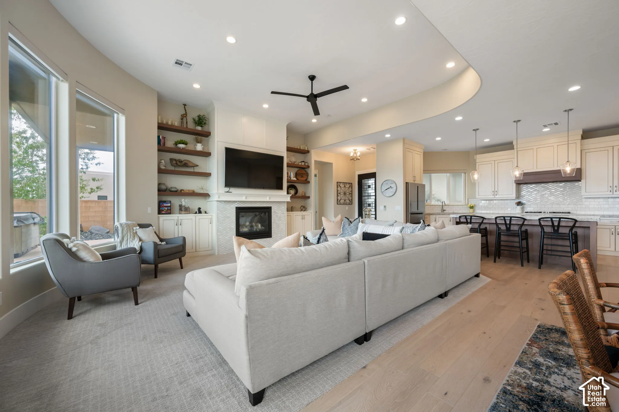 Open-concept living area featuring a kitchen island with seating, a fireplace with a stone-finish surround, custom built-in shelving, and recessed lighting