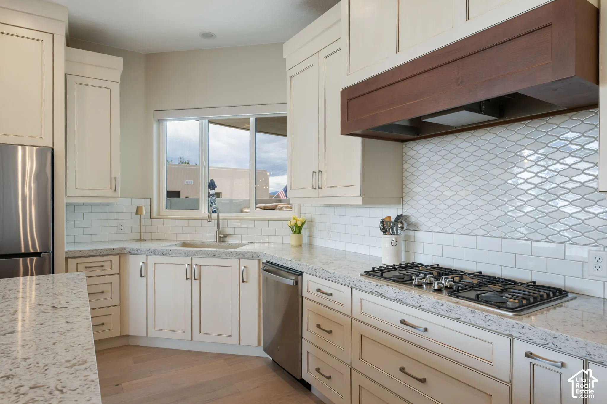 Kitchen featuring light-toned cabinetry, light-toned countertops, a stainless steel refrigerator, a gas cooktop, and wood-finish flooring