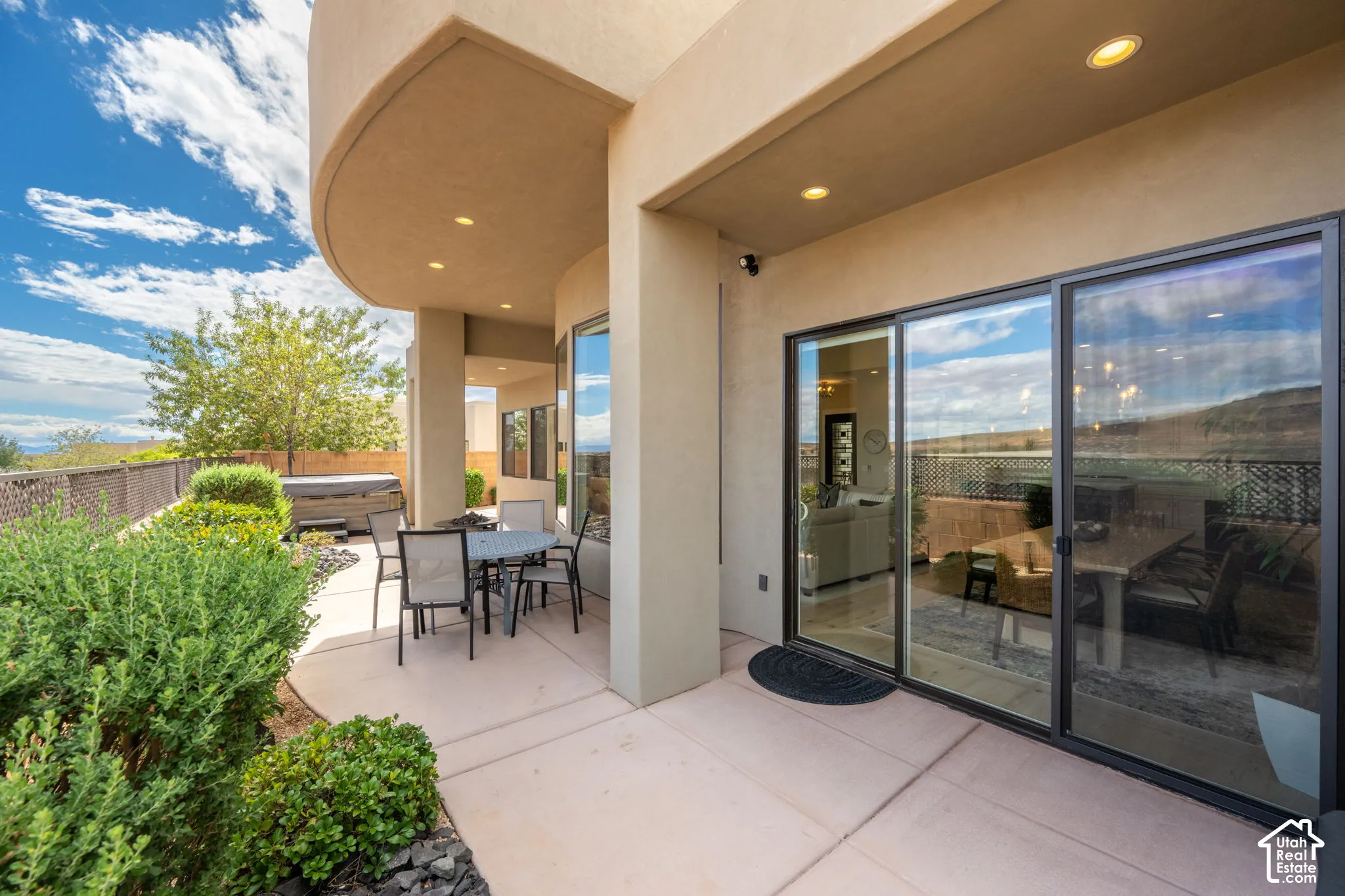 Curved stucco exterior with recessed lighting, large glass sliding doors, and a concrete patio