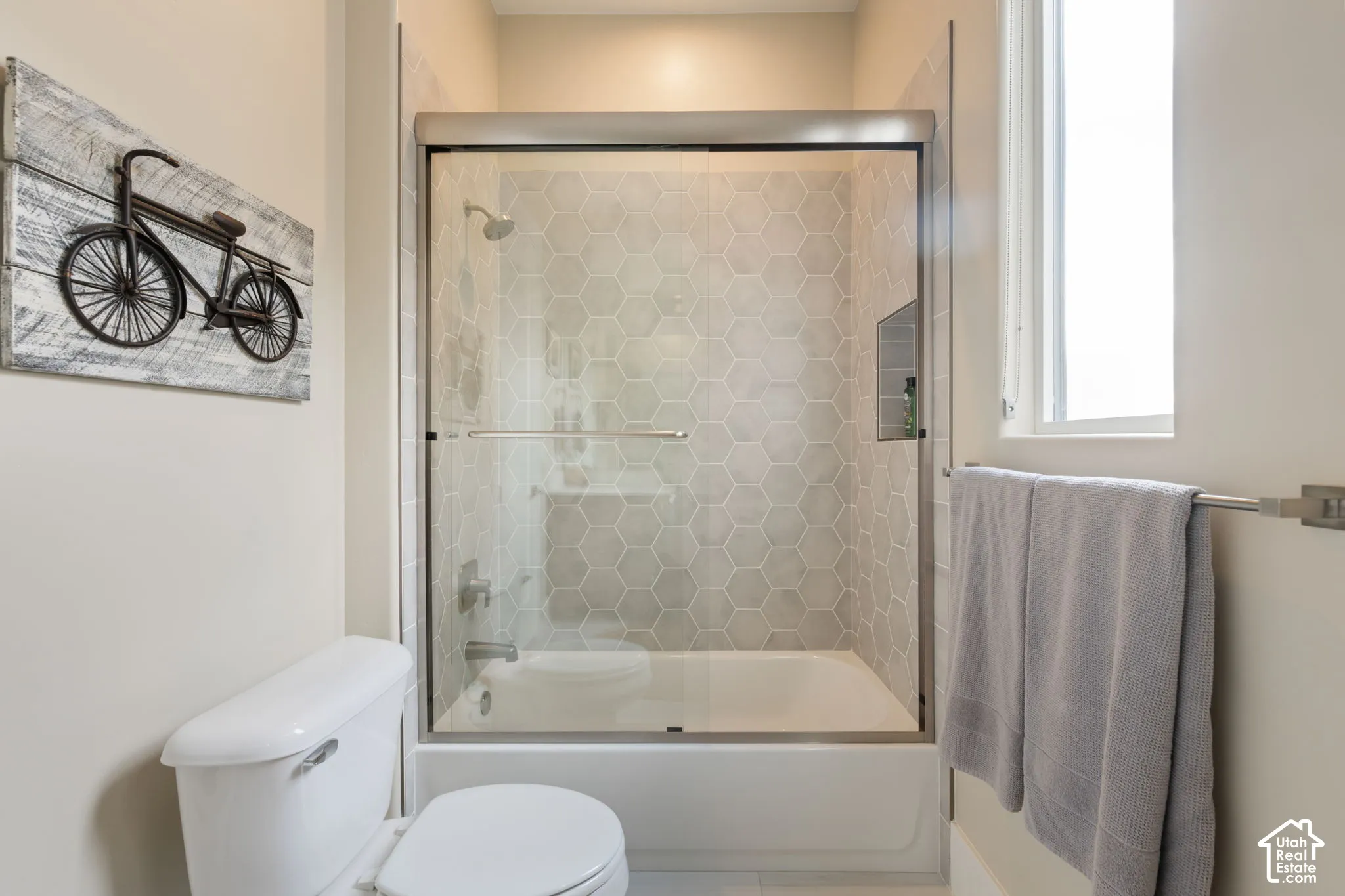 Bathtub and shower combination featuring hexagonal tile surround, glass sliding door, and a built-in shower niche