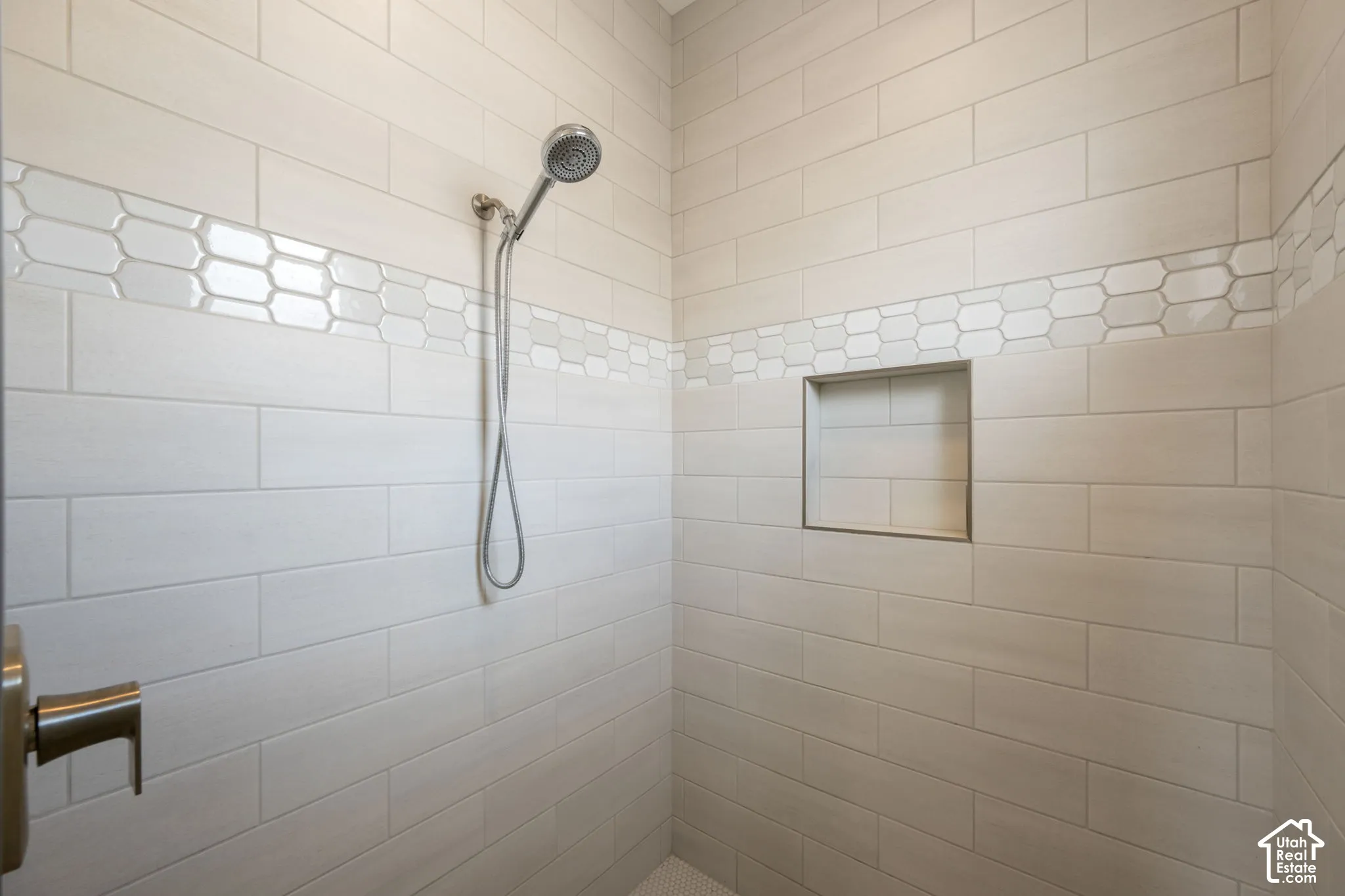 Subway tile shower surround with an accent band of hexagonal tiles, built-in shower niche, and a handheld shower fixture