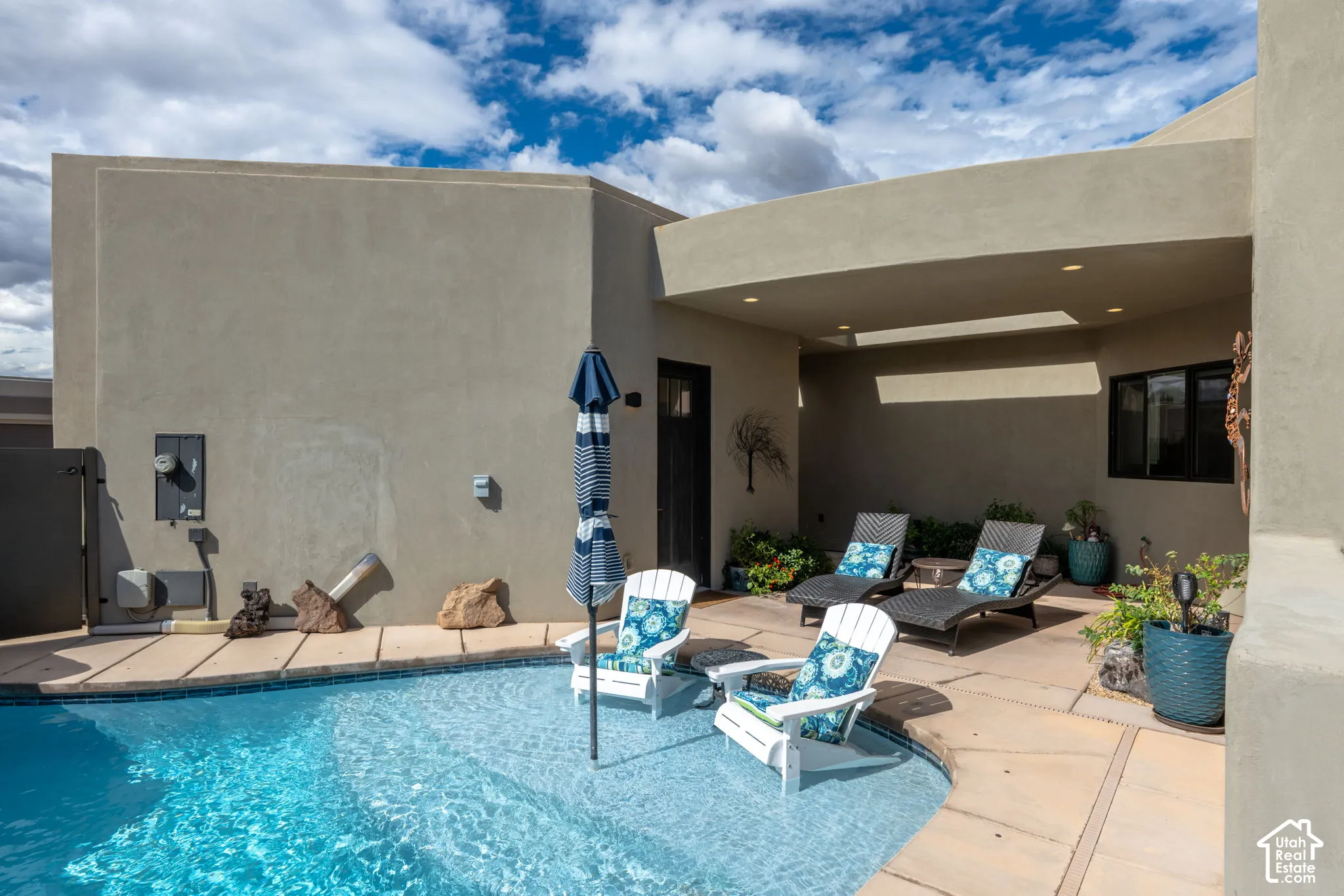 Curved pool with integrated seating, surrounded by a stone patio and stucco exterior