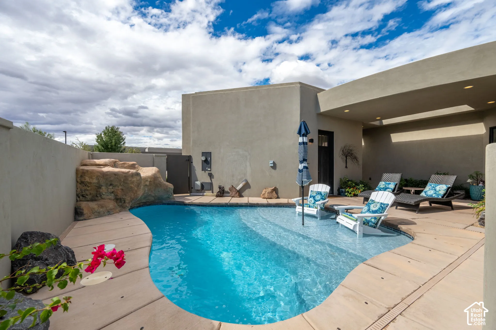 Private backyard pool featuring a rock waterfall, integrated tanning ledge, and covered patio area with recessed lighting