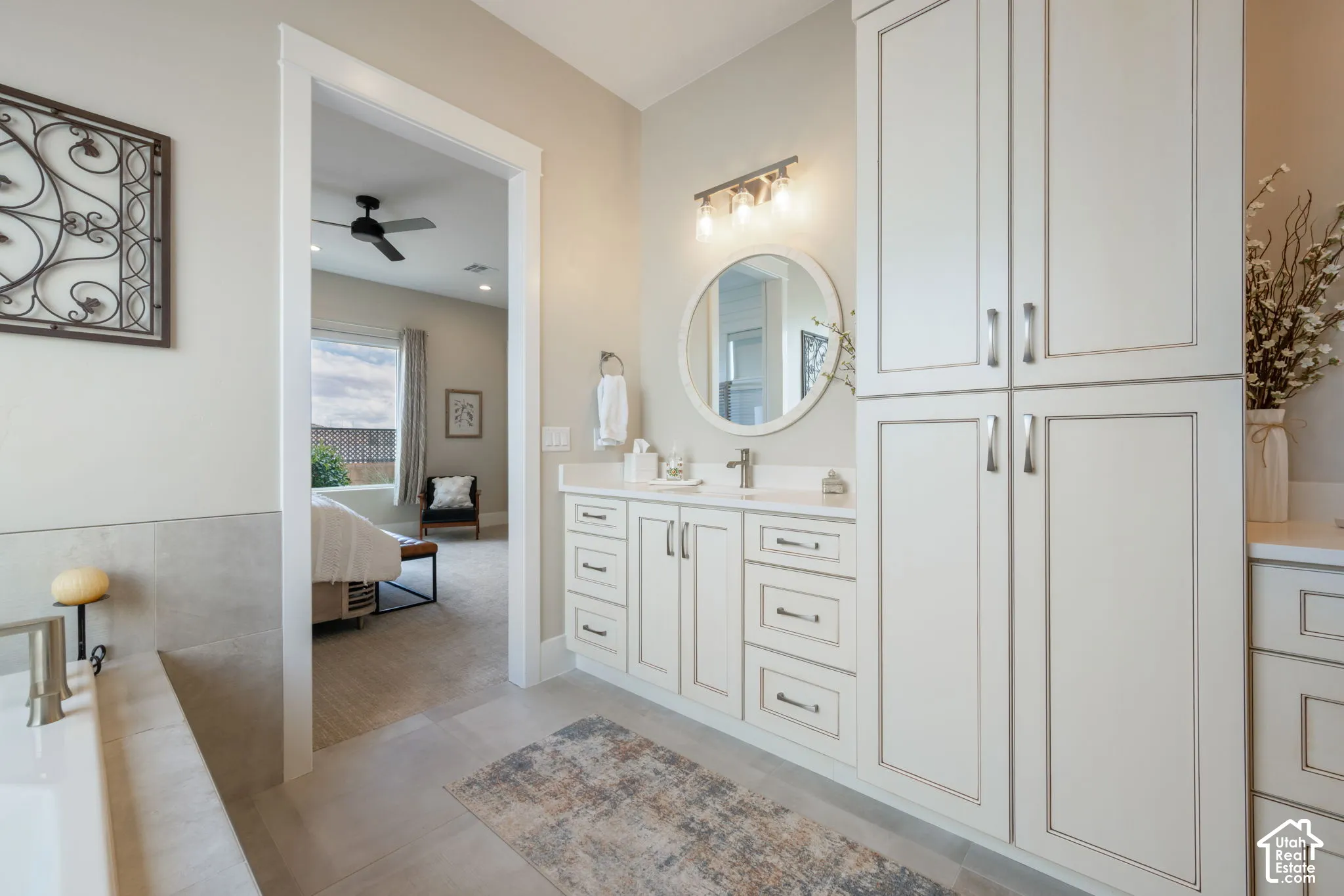 Dual vanities with white cabinetry, white countertops, a built-in soaking tub, and floor-to-ceiling storage cabinetry