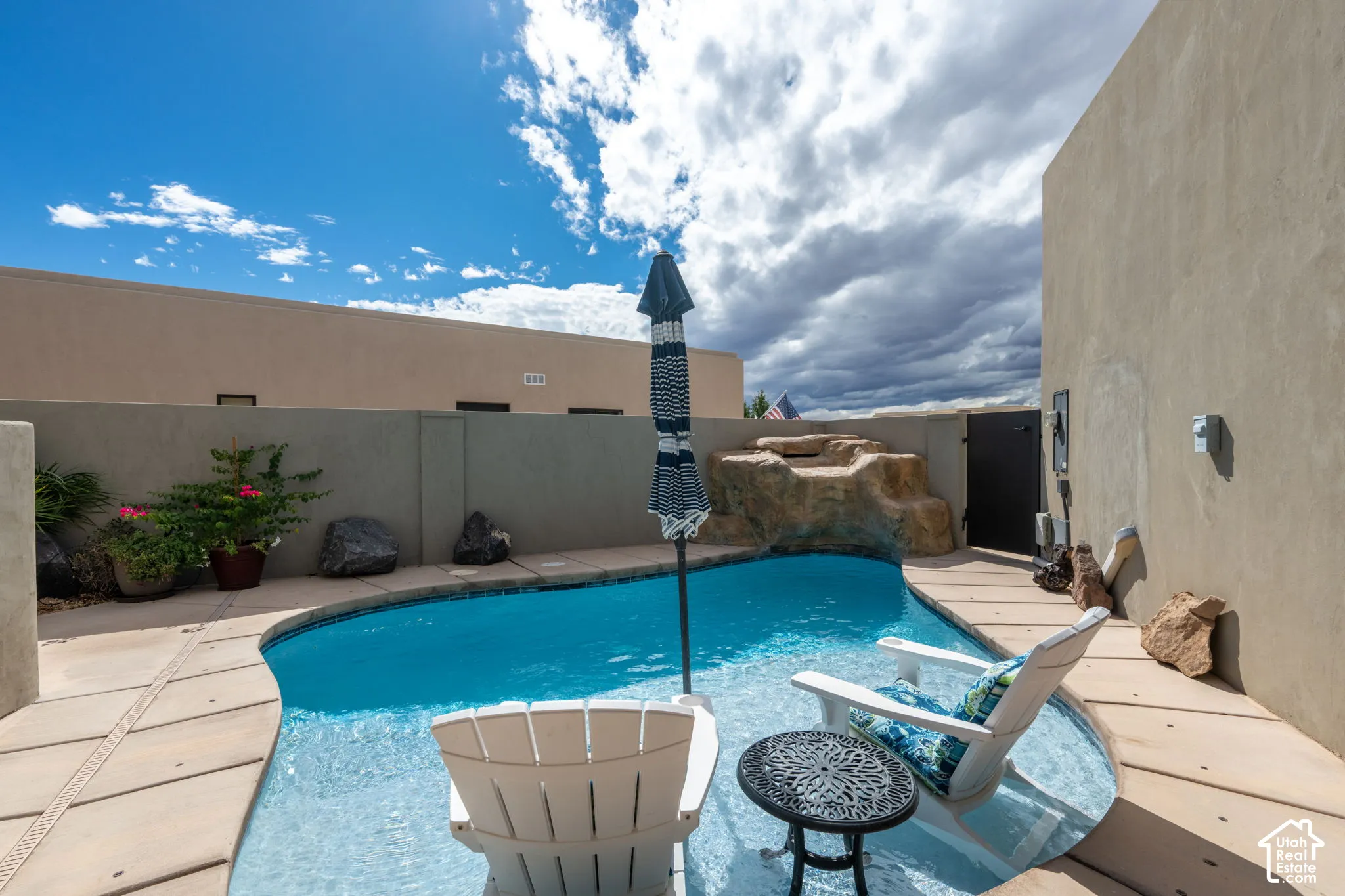Curved swimming pool with an integrated rock waterfall feature, surrounded by concrete paver decking