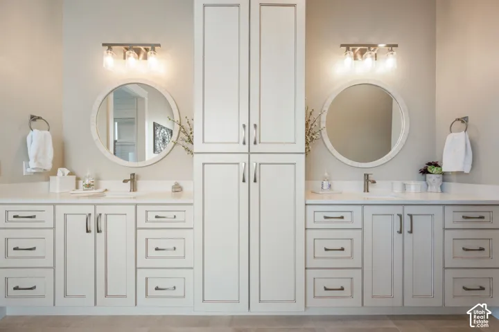 Dual vanity featuring white cabinetry with brushed nickel hardware, white countertops, and circular framed mirrors