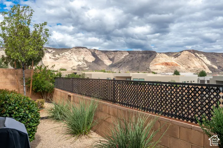 Lattice-patterned metal fencing with a concrete block retaining wall, desert landscaping featuring gravel and various plants, and distant mountainous terrain