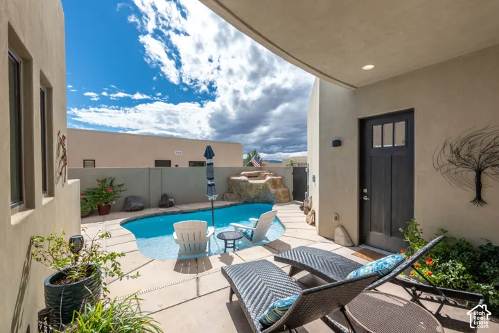 Private courtyard featuring a curvilinear pool with stone water feature, stucco exterior, and dark wood-finish entry door with clear glass panels