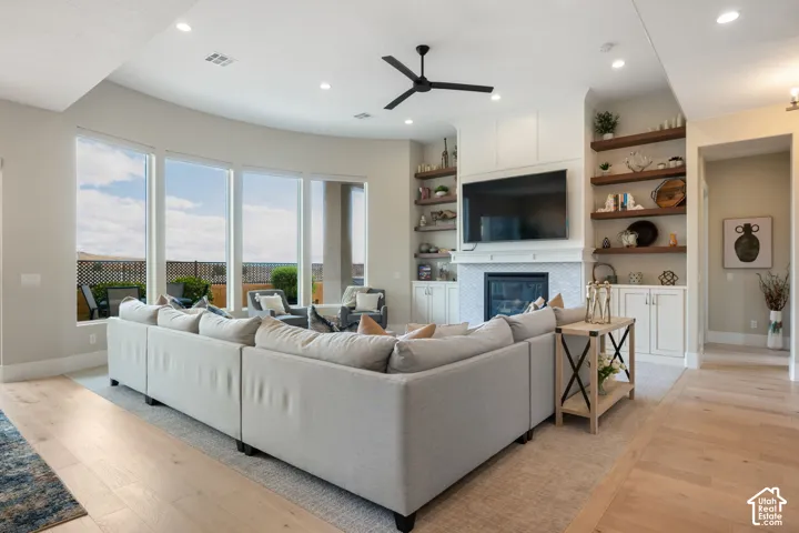 Spacious living area featuring large windows, wood-finish flooring, a ceiling fan, and built-in shelving with a fireplace