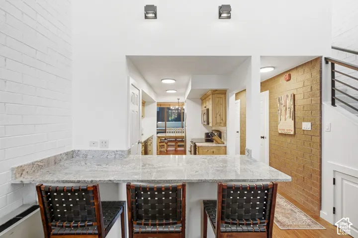 Breakfast bar with a stone countertop, white brick wall, and wood-finish flooring
