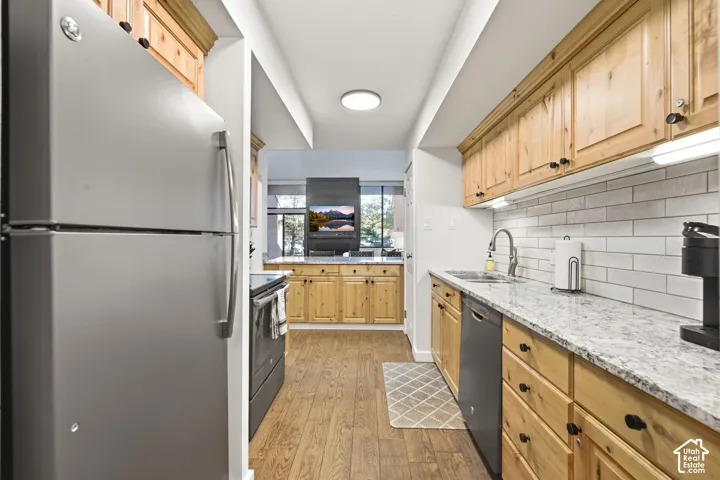 Galley kitchen featuring wood-finish flooring, light wood cabinetry, white subway tile backsplash, and light-toned countertops