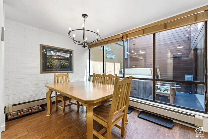 White brick accent wall with a contemporary chandelier, large windows, wood-finish flooring, and a private outdoor space