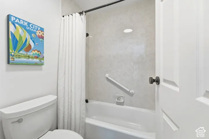 Built-in bathtub with shower, wall-mounted grab bar, and recessed lighting