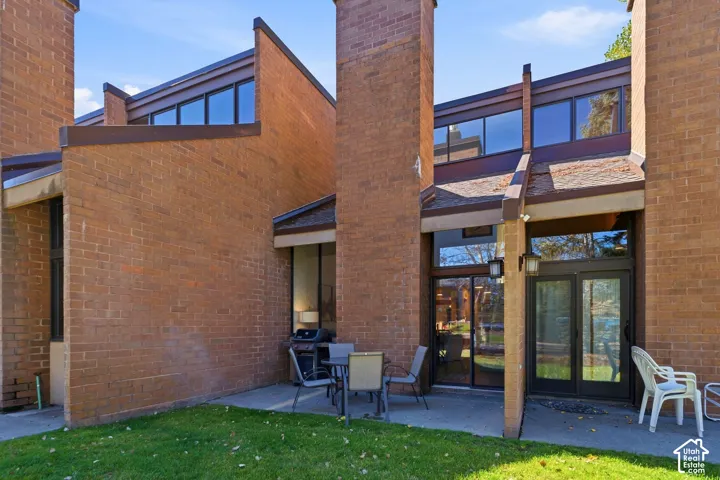 Brick exterior with multiple large windows, a ground-level patio, and a grassy area