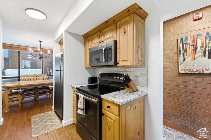 Wood-finish flooring, light wood cabinetry, white subway tile backsplash, stainless steel appliances, and light-colored granite countertops