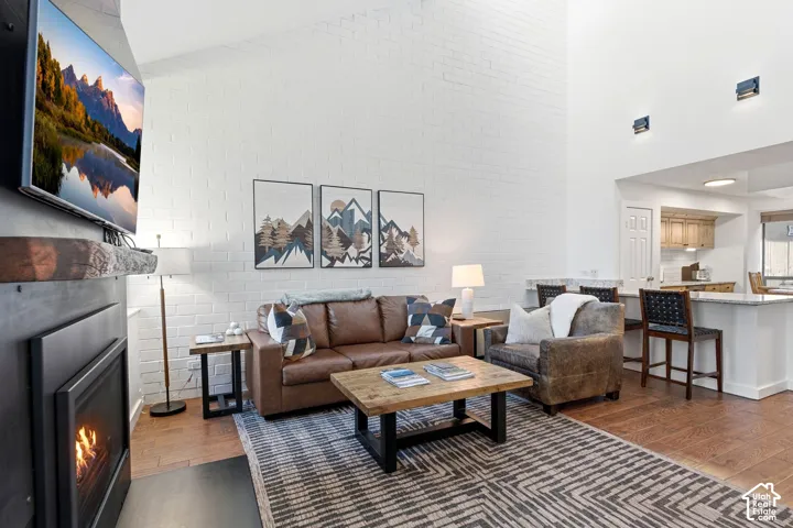 Soaring vaulted ceiling, white brick accent wall, wood-finish flooring, built-in fireplace, and a breakfast bar with seating