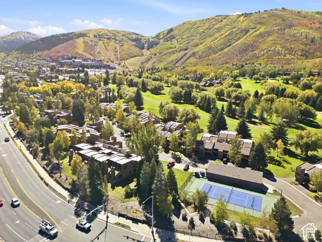 Terraced residential structures, mature trees, golf course, mountain backdrop, and tennis court with surrounding hardscaping