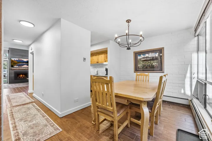 Wood-finish flooring throughout, a dining area featuring a chandelier and white brick accent wall, and a living area with a built-in fireplace and media console