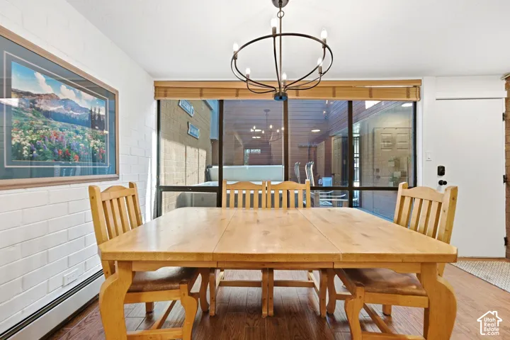 Wood-finish flooring, white brick accent wall, large windows with natural light, and a black metal chandelier