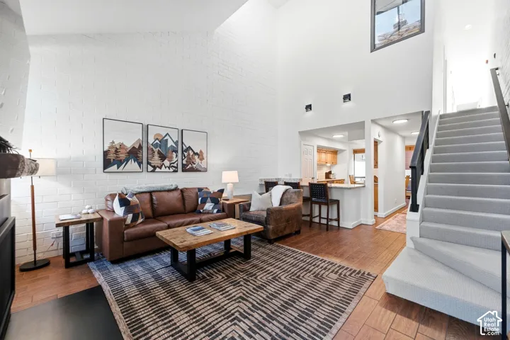 Vaulted ceilings, white-painted brick accent wall, wood-finish flooring, built-in breakfast bar, and carpeted staircase