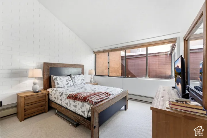Sloped ceiling with white brick accent wall, wood-finish flooring, and large windows with privacy blinds