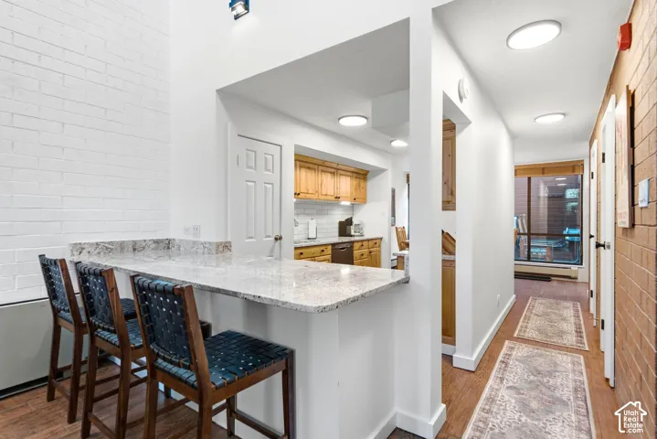 Breakfast bar with a light-toned countertop, exposed brick accent wall, wood-finish flooring, recessed lighting, and natural wood cabinetry