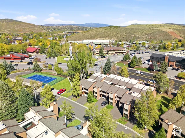 Terraced residential buildings with pitched roofs, surrounded by mature trees, and a visible tennis court