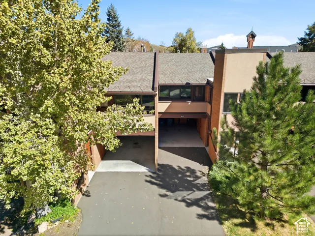 Townhome exterior with a brick and stucco facade, featuring covered carport parking, asphalt driveways, and mature landscaping