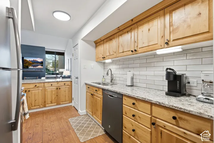 Kitchen featuring wood-finish cabinetry, light-toned granite countertops, a subway tile backsplash, stainless steel appliances, and wood-finish flooring