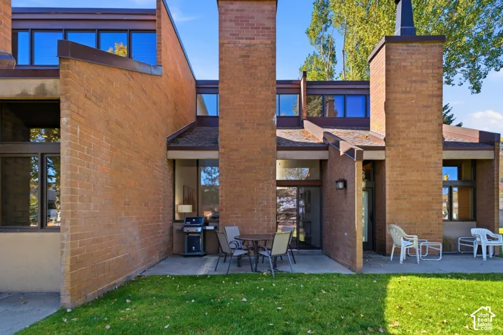 Brick exterior with multiple large windows, a ground-level patio, and a manicured lawn