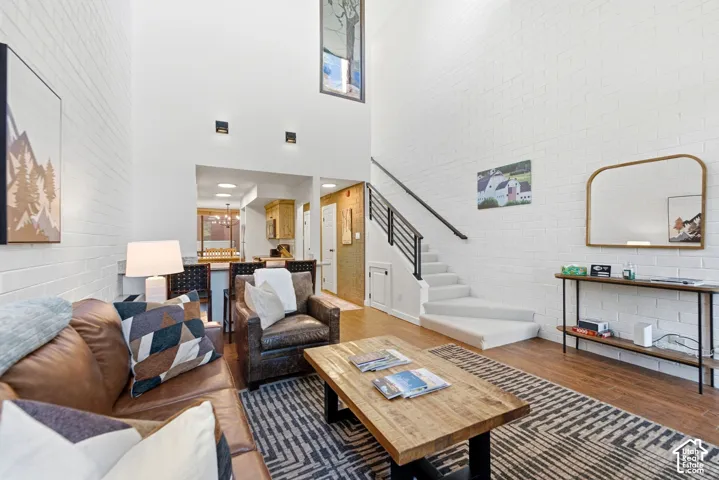 High ceilings with recessed lighting, white painted brick accent wall, wood-finish flooring, a carpeted staircase with dark metal railings, and a built-in bar area with stone countertops