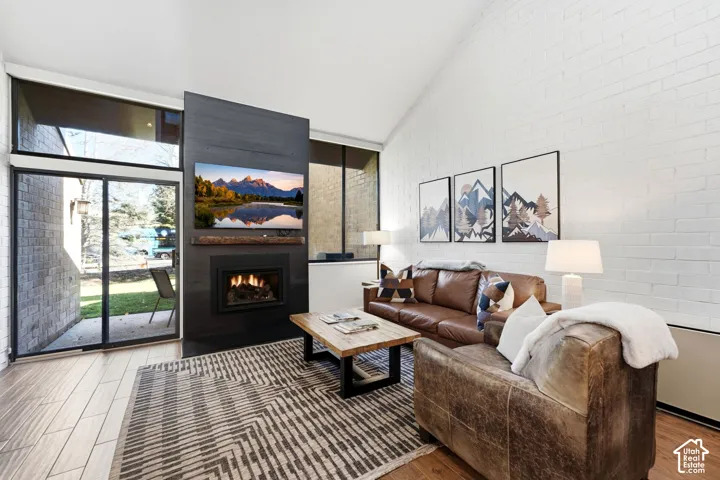 Vaulted ceiling with white painted brick, wood-finish flooring, built-in fireplace, and sliding glass door with transom window