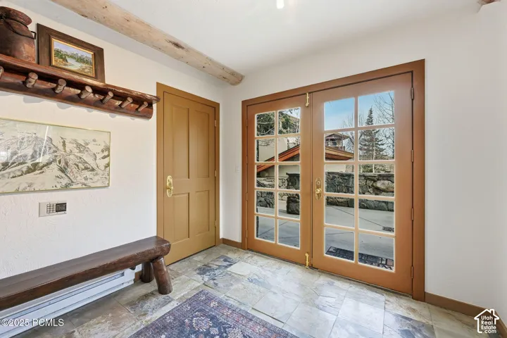 French doors with multiple lites, natural wood beam ceiling accent, stone tile flooring, and a built-in wooden coat rack
