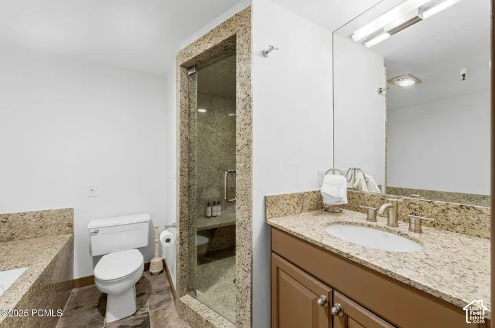 Bathroom featuring a glass-enclosed shower with a built-in bench, a toilet, a vanity with a drop-in sink, and a large wall mirror