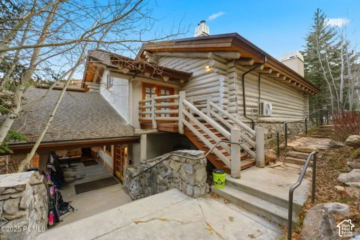Log cabin exterior with stone foundational elements, a natural wood deck with railing, and a covered entryway